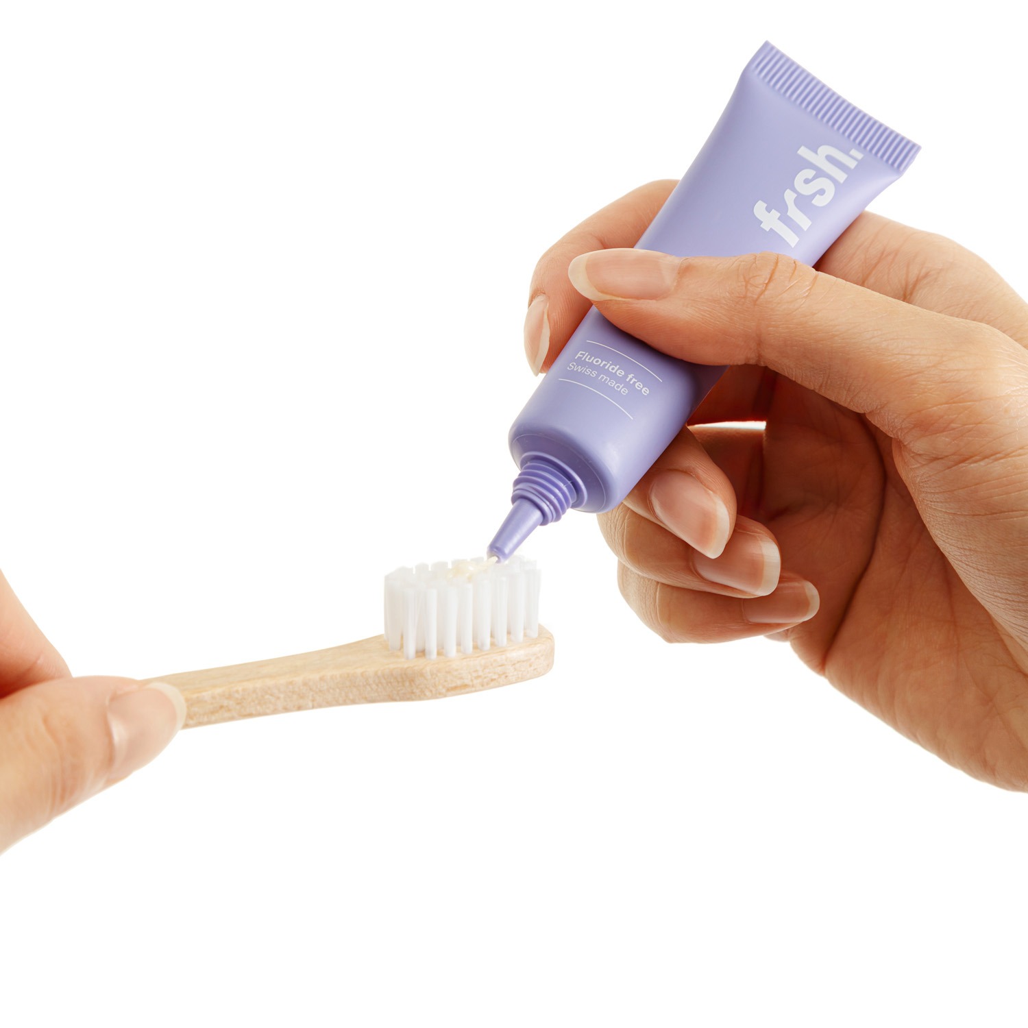 Nahaufnahme einer Person, die fluoridfreie Zahnpasta auf eine Bambuszahnbürste aufträgt